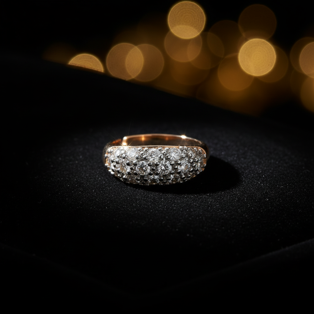 A gold ring with a pavé-set row of clear gemstones, displayed on a black textured surface with warm golden bokeh lights in the background.