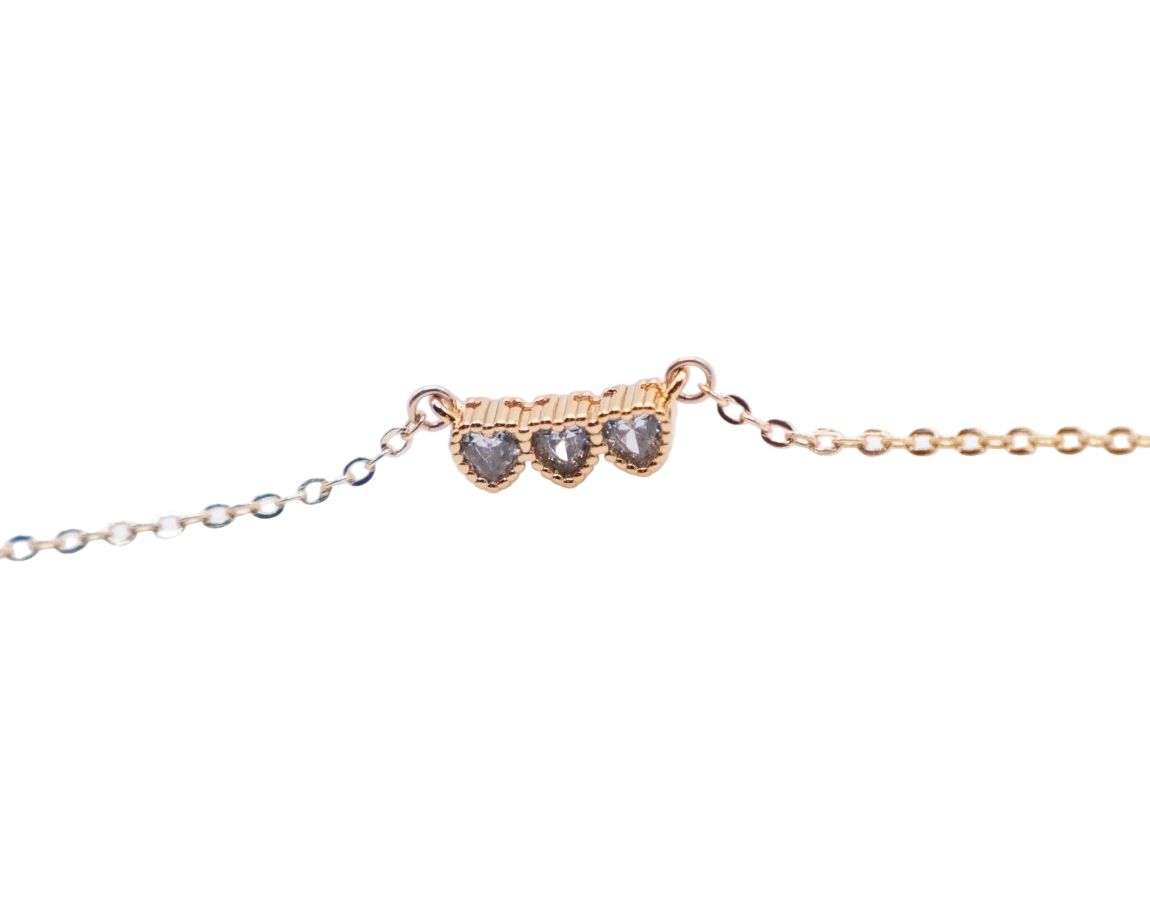 Dainty gold necklace with three heart-shaped gemstones on a white background