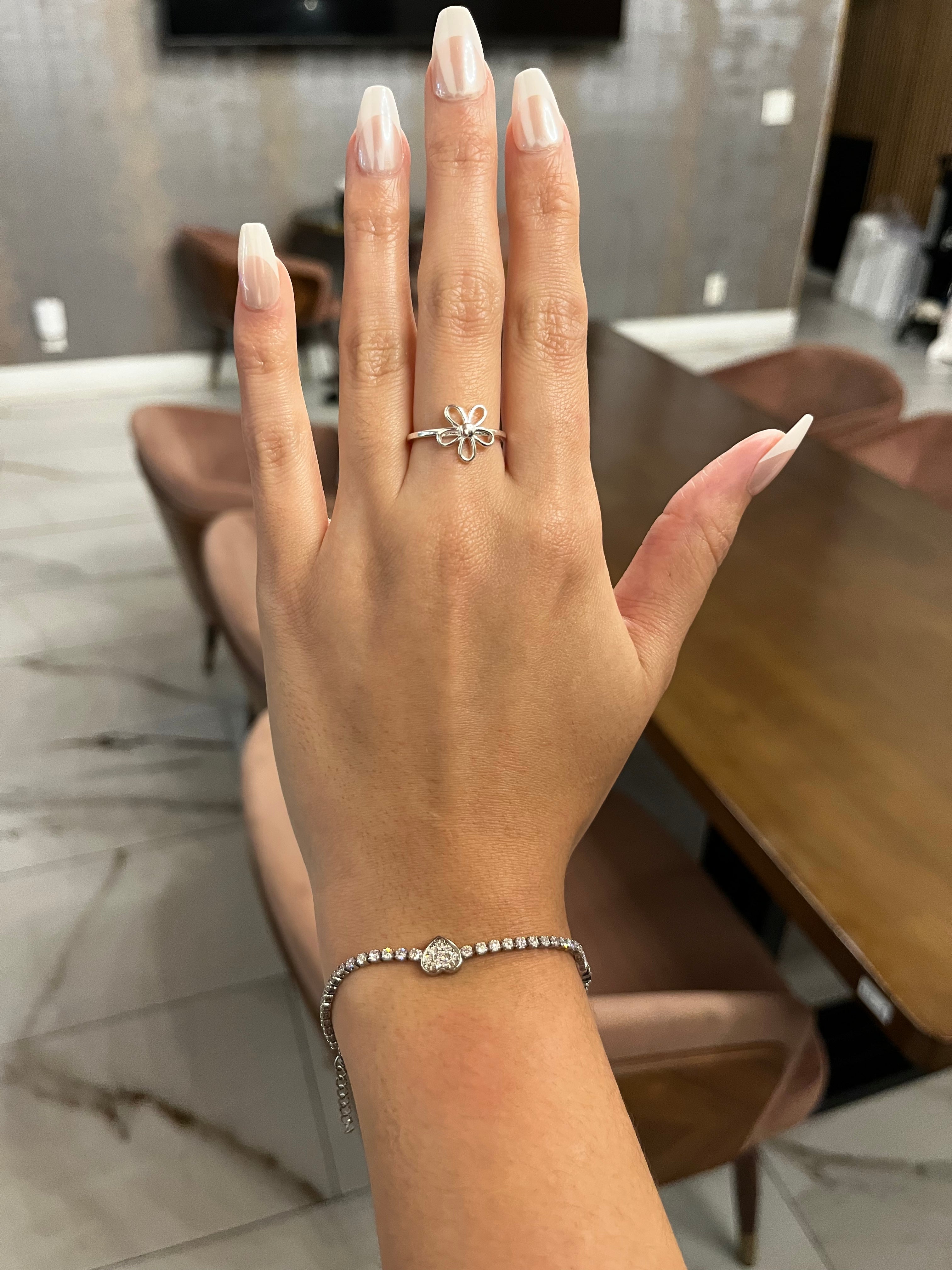 Hand wearing a silver ring with a flower design and a bracelet, blurred background