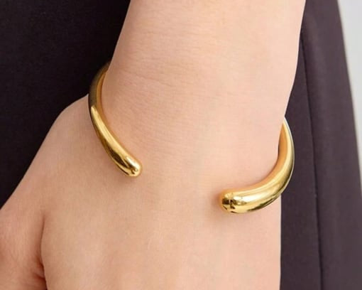 Gold bangle on a wrist with a neutral background
