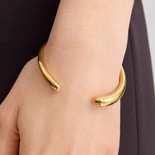 Gold bangle on a wrist with a neutral background