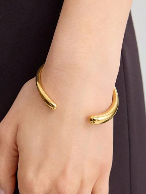 Gold bangle on a wrist with a neutral background