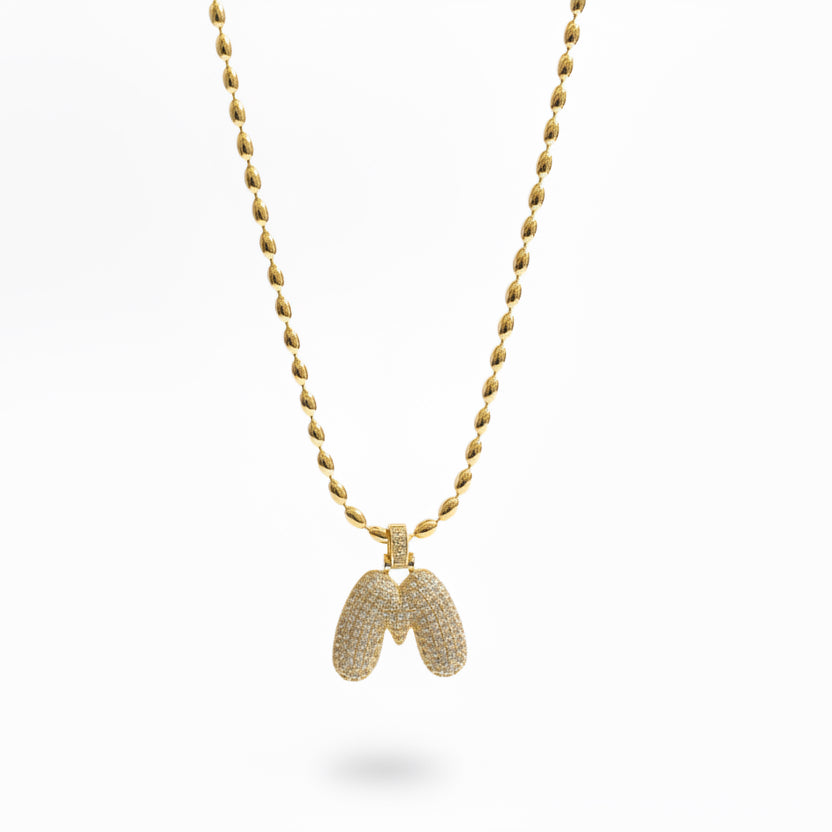 Gold chain necklace with a bubble letter pendant against a white background.