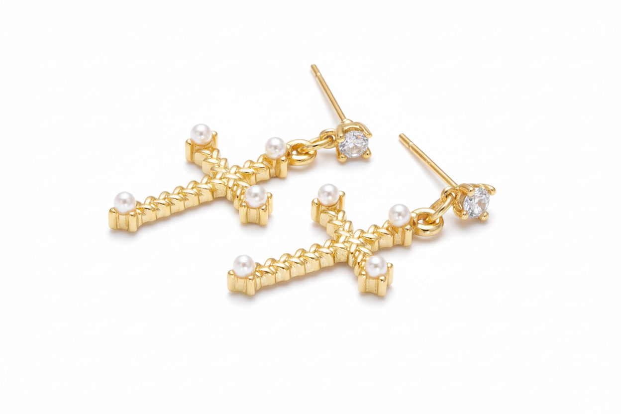 Gold cross-shaped earrings with pearls and clear stones on a white background