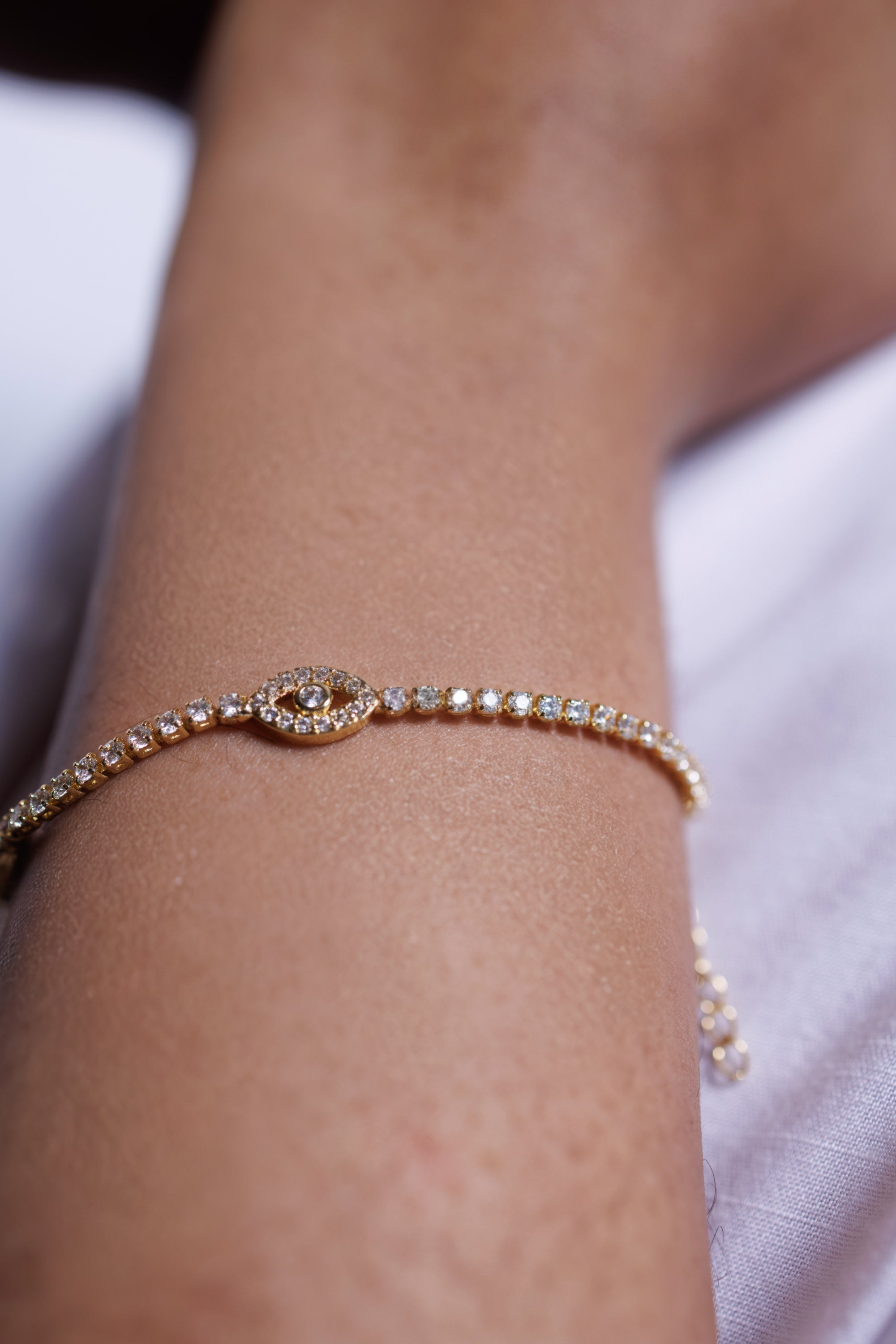 Gold tennis bracelet with clear stones on a wrist against a light background