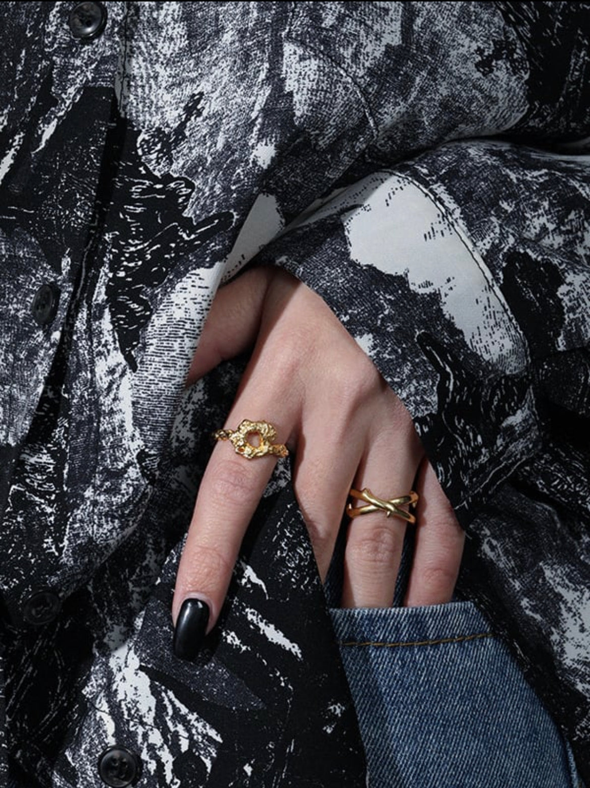 Close-up of a hand wearing two gold rings on a textured black and gray background