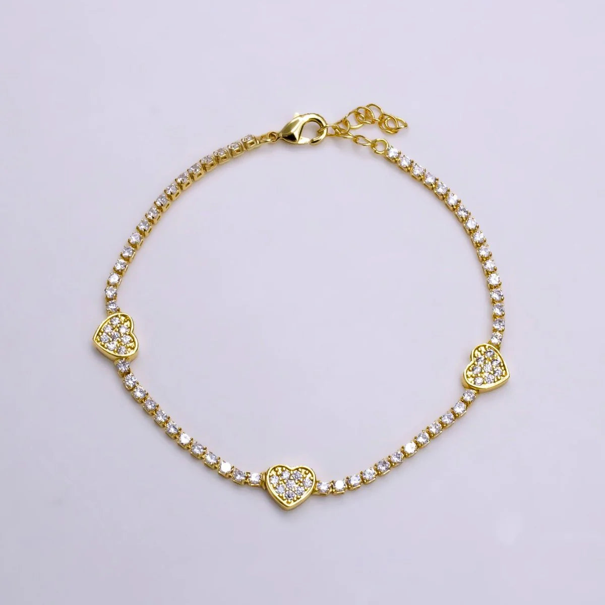 Gold bracelet with heart-shaped charms on a light gray background