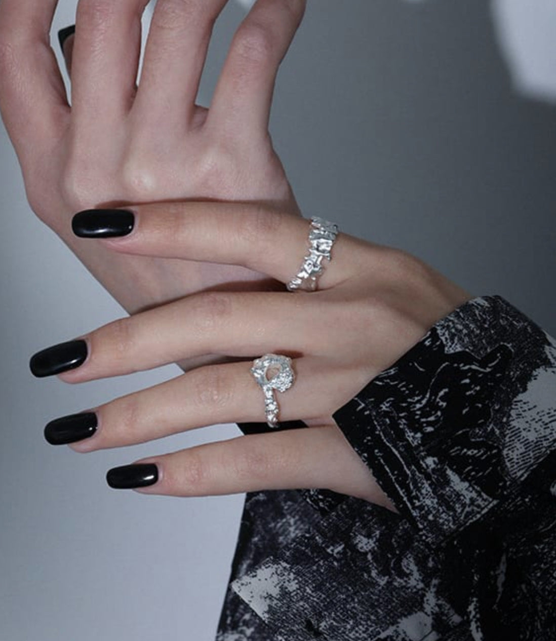 Close-up of a hand wearing two silver rings with a plain background