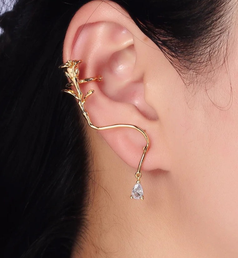 Gold ear cuff with a teardrop-shaped gemstone worn by a person.
