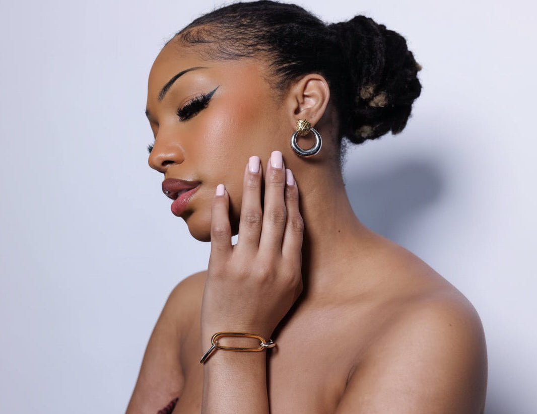 Woman wearing gold hoop earrings and bracelet against a light background