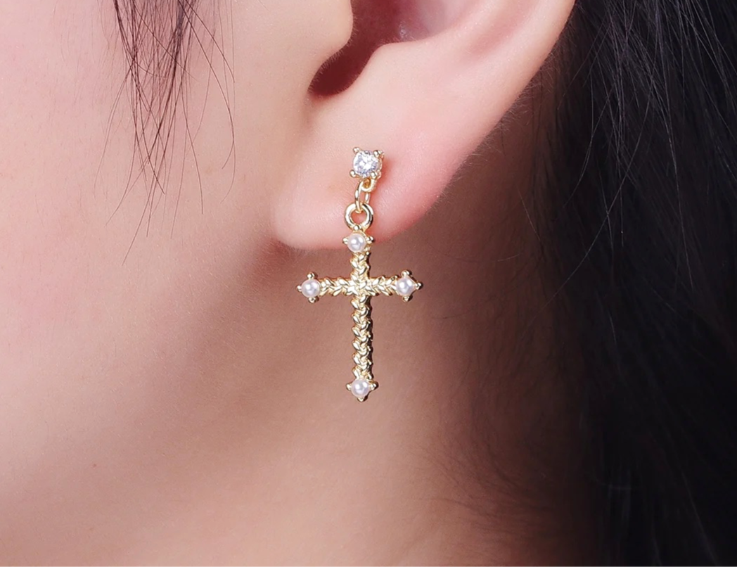 Gold cross earring with clear stones worn by a person