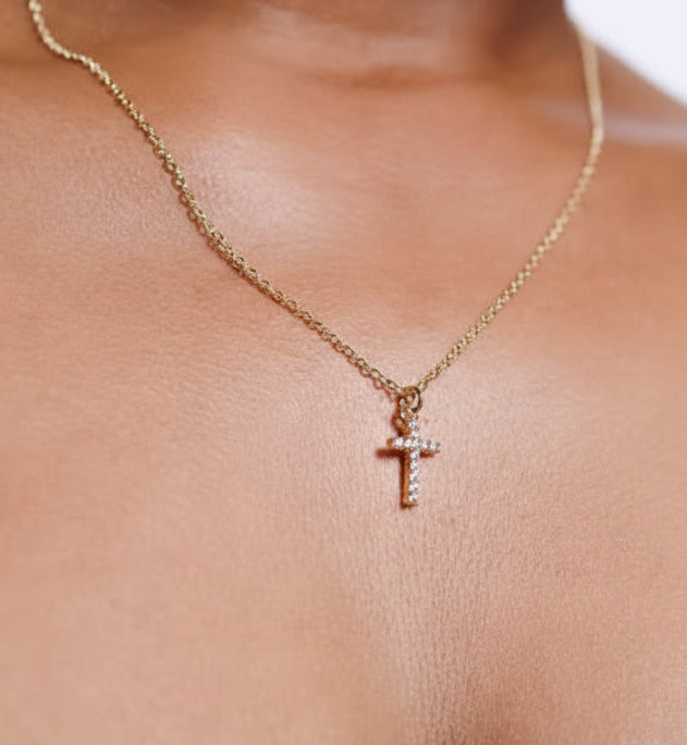 Gold necklace with a cross pendant on a person wearing a black top.
