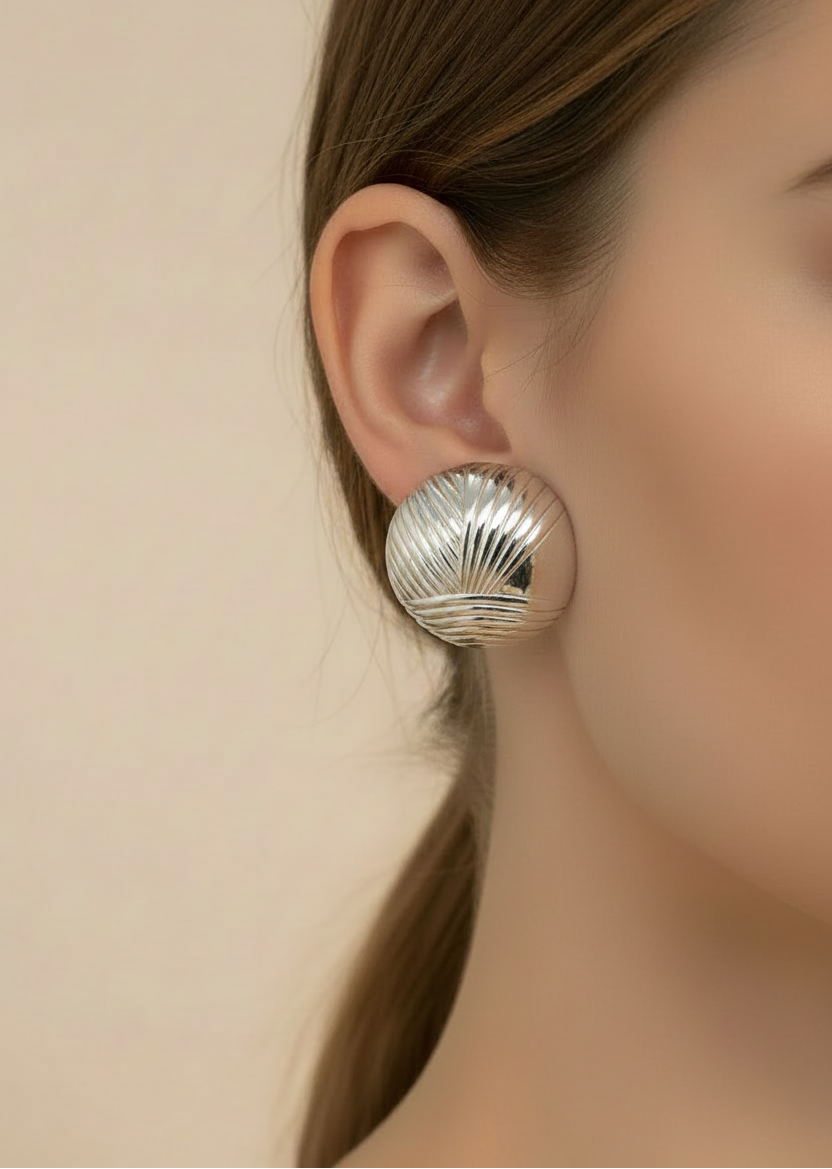Silver shell-shaped earring worn by a person with a neutral background