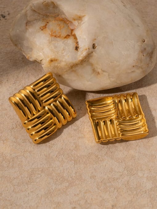 Two gold textured square pendants on a stone surface
