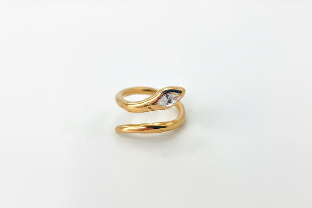 A gold snake ring with a small clear marquise-cut gemstone on its head, photographed on a plain white background.
