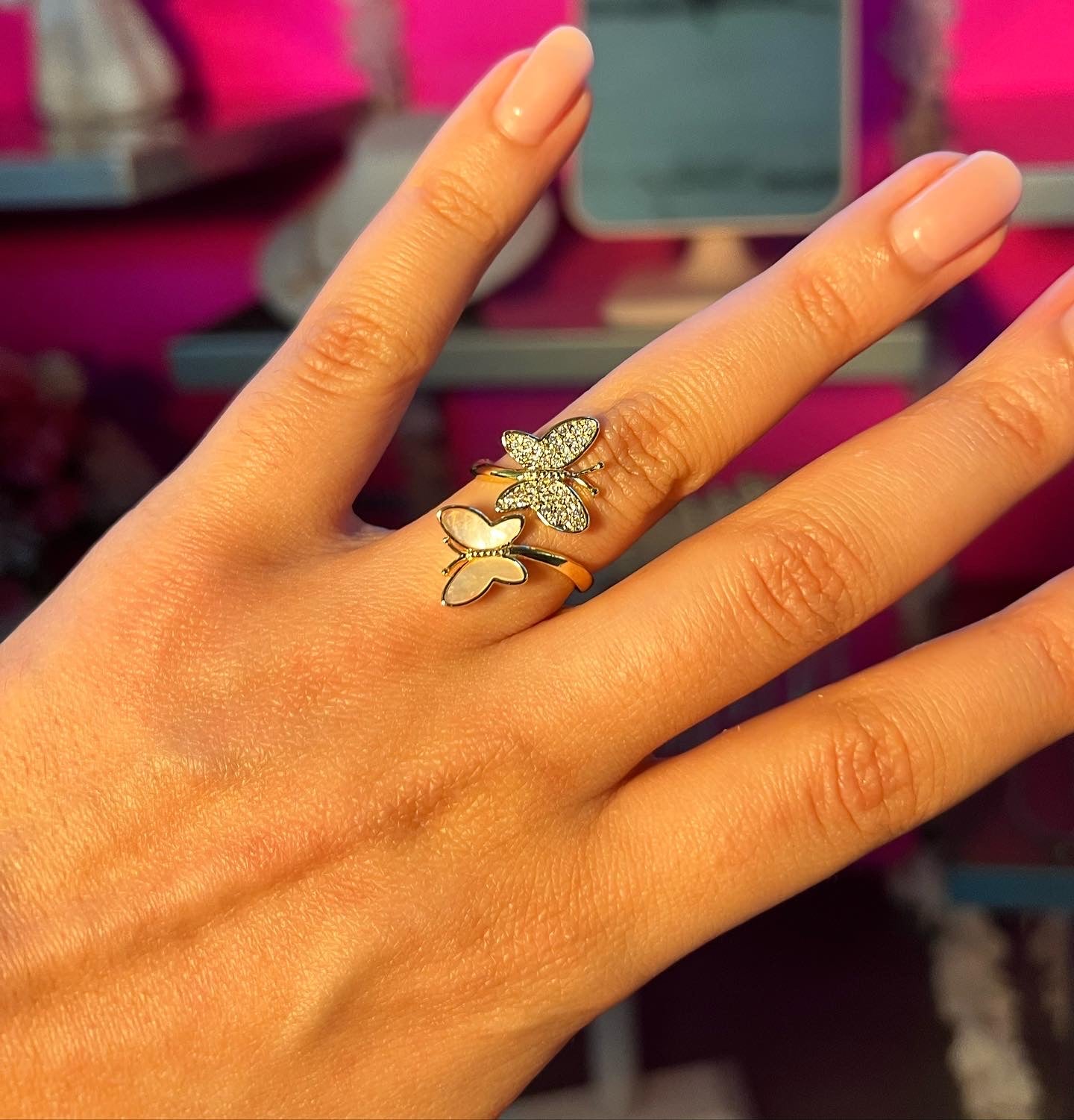 Hand wearing two butterfly-themed rings with a blurred background