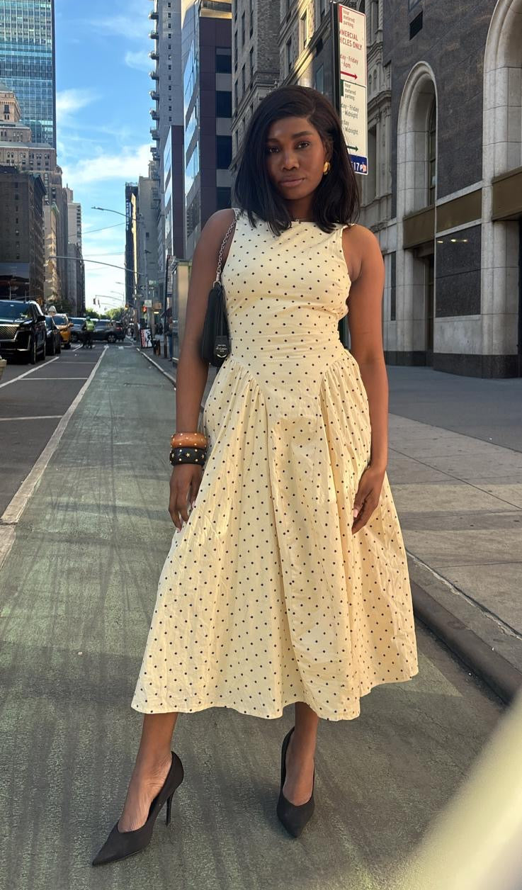 Woman in a light-colored dress standing on a city street with tall buildings.