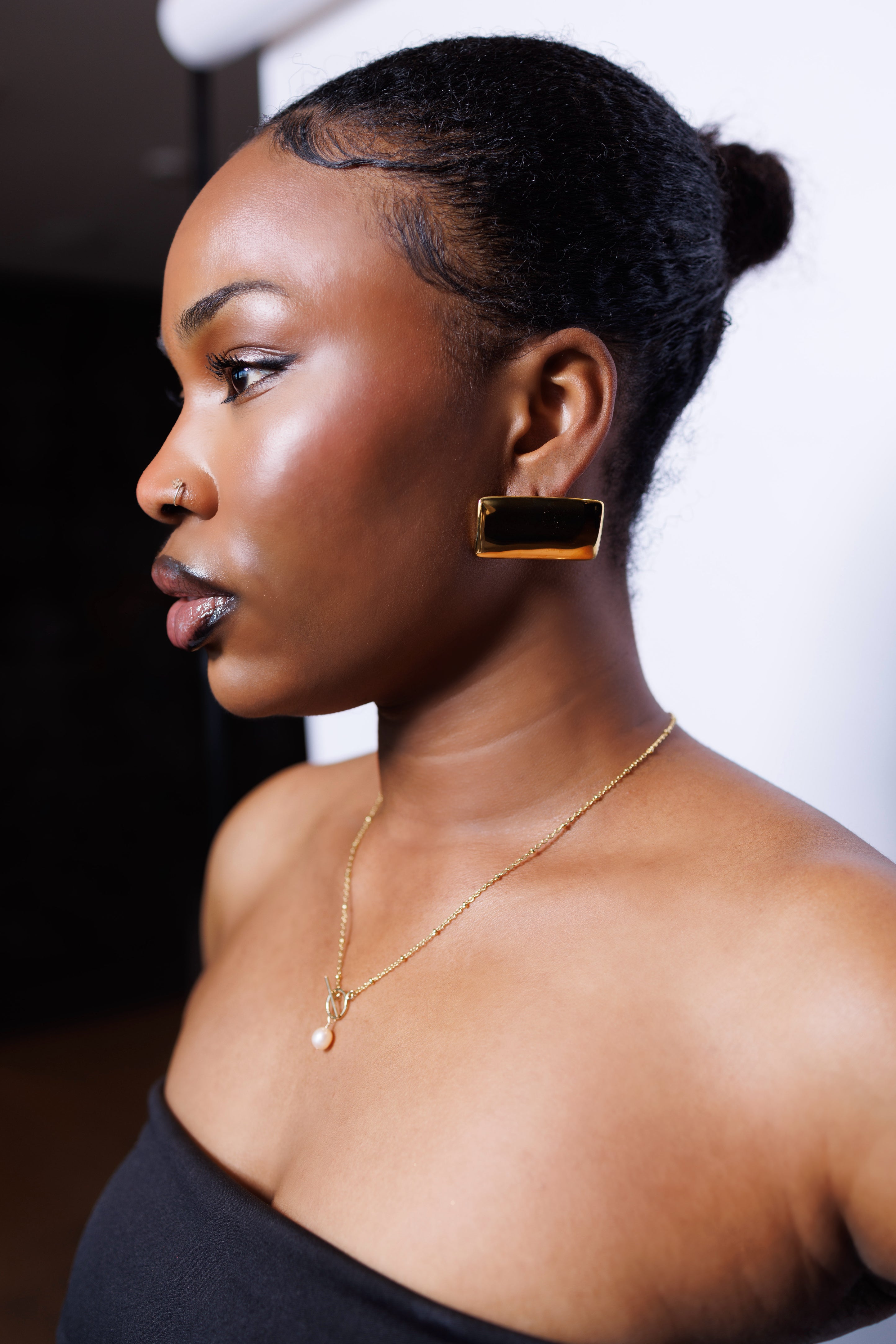 Woman wearing gold earrings and necklace against a white background
