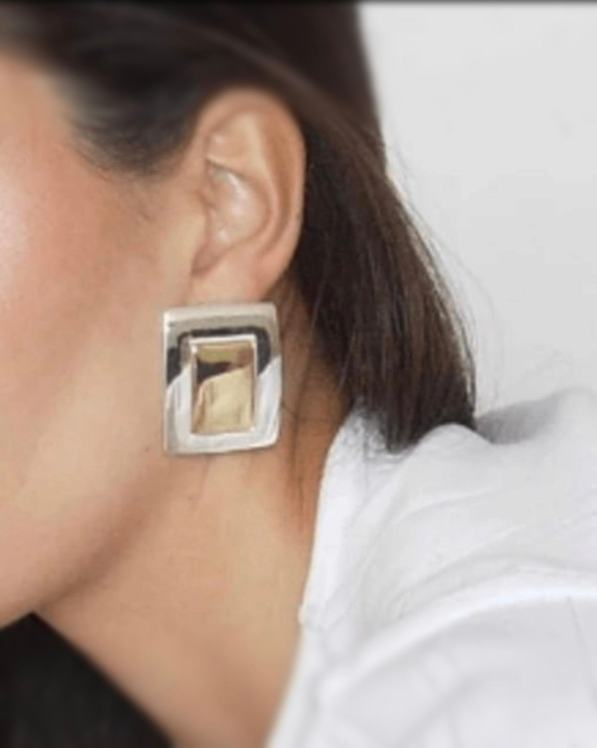 Close-up of a person wearing a silver square earring with a beige center.