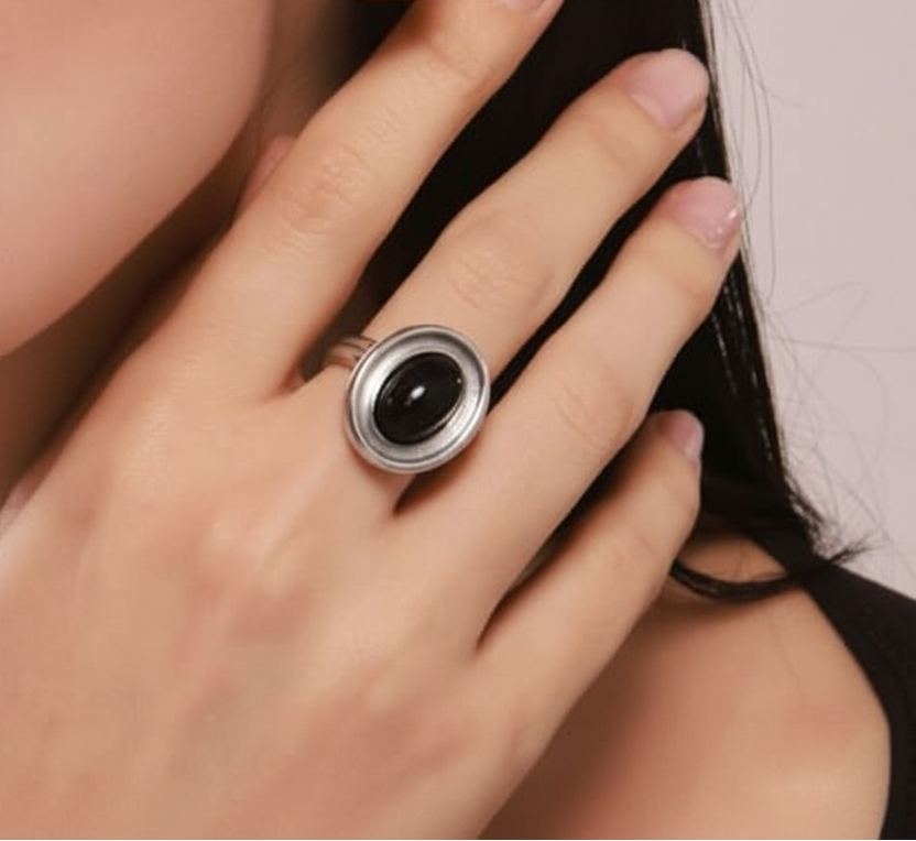 A close-up of a hand wearing a silver ring with a large oval black stone.