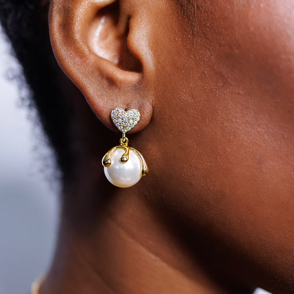 Close-up of an ear wearing a pearl earring with a heart-shaped top.
