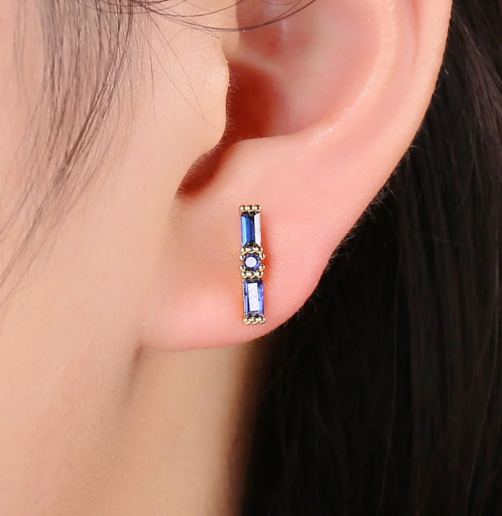 Close-up of an ear wearing a blue gemstone earring with gold accents.