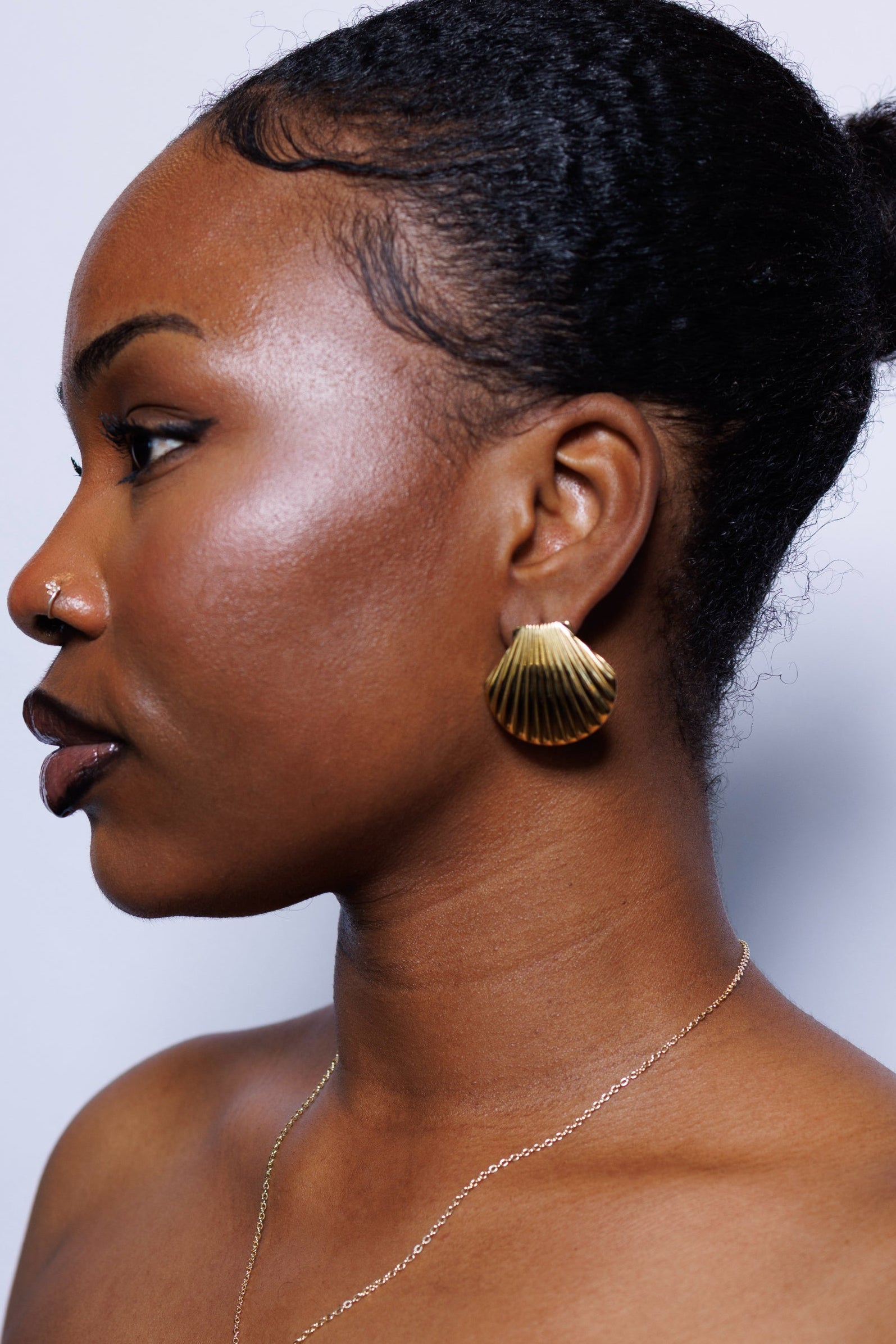 Woman wearing gold earrings and a black top against a light background