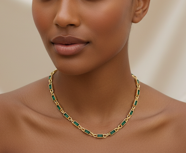 Woman wearing a gold and green necklace against a neutral background
