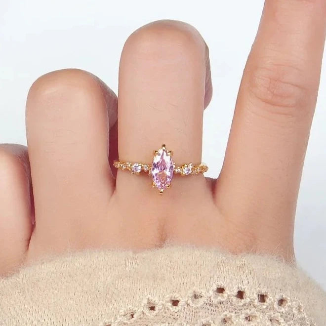 Hand wearing a gold ring with a pink gemstone on a white background