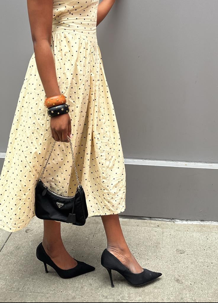 Woman in a beige polka dot dress standing against a gray wall.