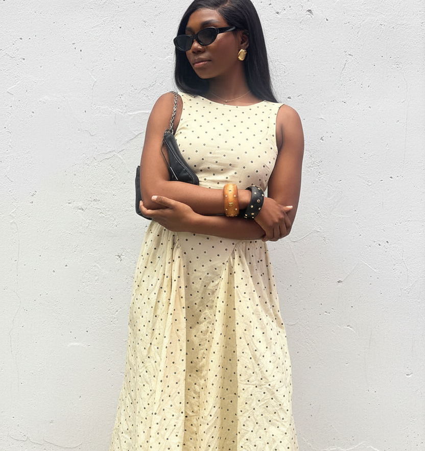 Woman in a yellow polka dot dress standing against a white wall.