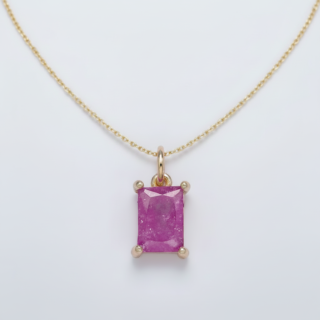 Gold pendant with a pink gemstone on a light gray background