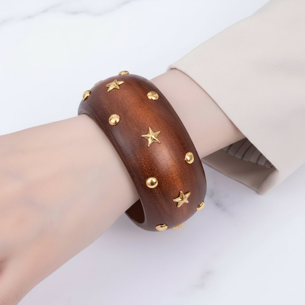 Wooden bracelet with gold star and circle studs on a wrist against a light background