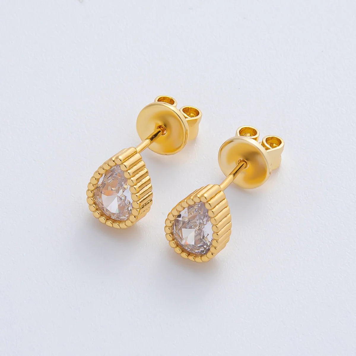 Gold earrings with clear gemstones on a light gray background