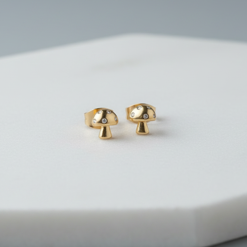 Gold mushroom-shaped earrings on a white surface with a gray background
