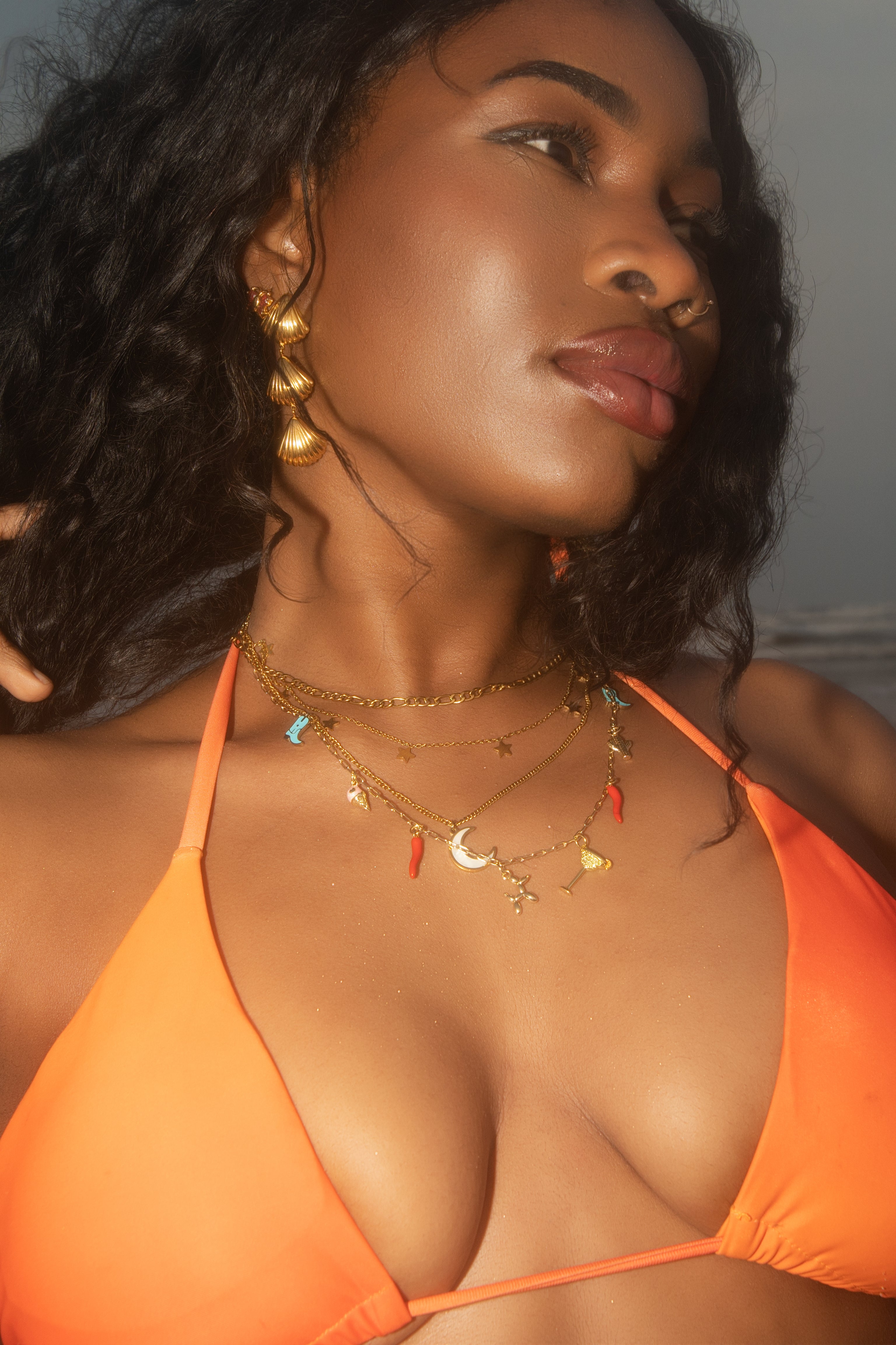 Woman wearing an orange bikini with gold jewelry against a neutral background