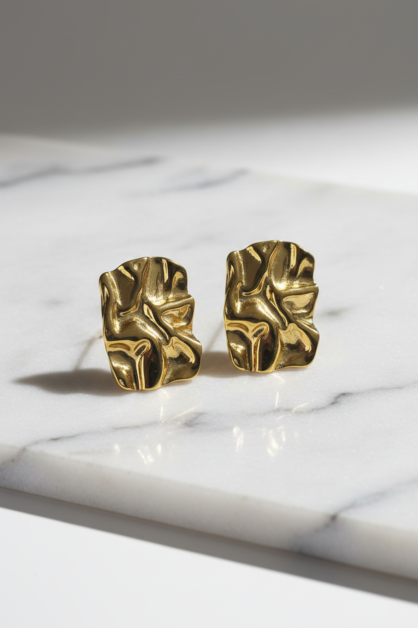 Gold leaf-shaped earrings on a marble surface