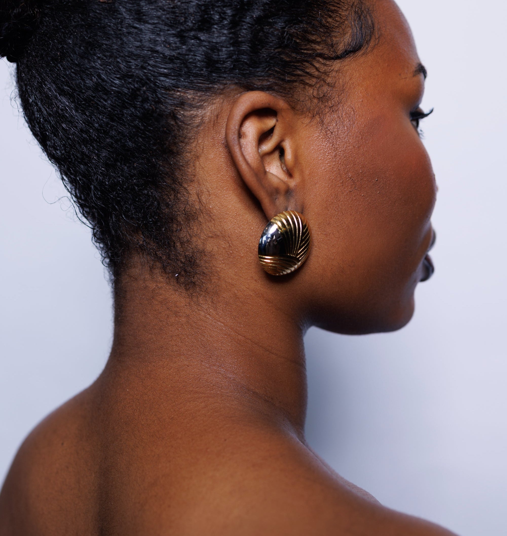 Side profile of a woman with braided hair wearing gold earrings against a white background