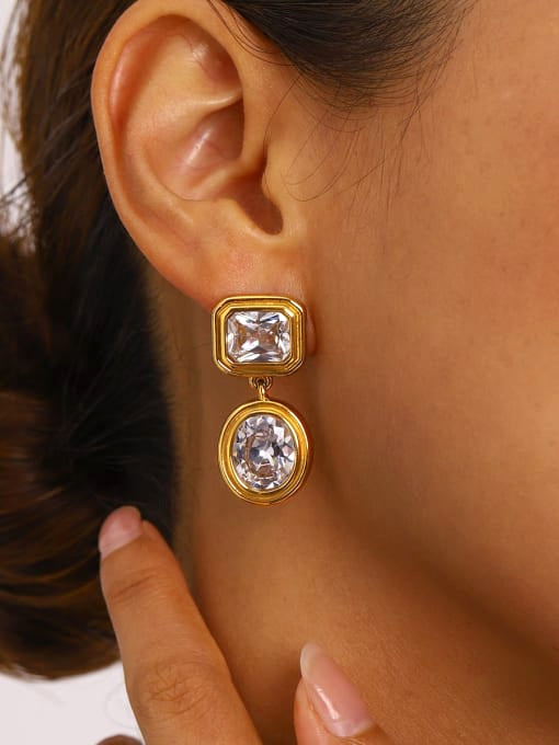 Close-up of a person wearing gold earrings with clear stones.