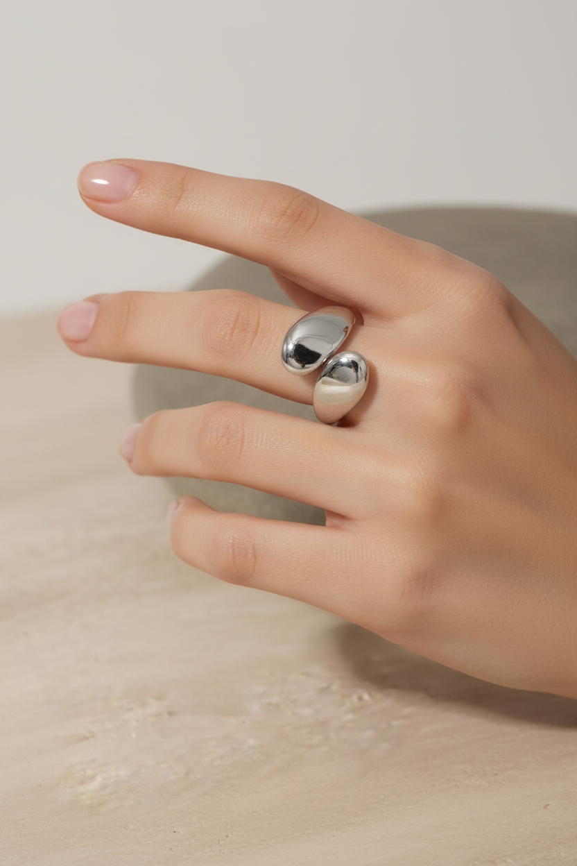 Hand wearing two silver rings on a neutral background