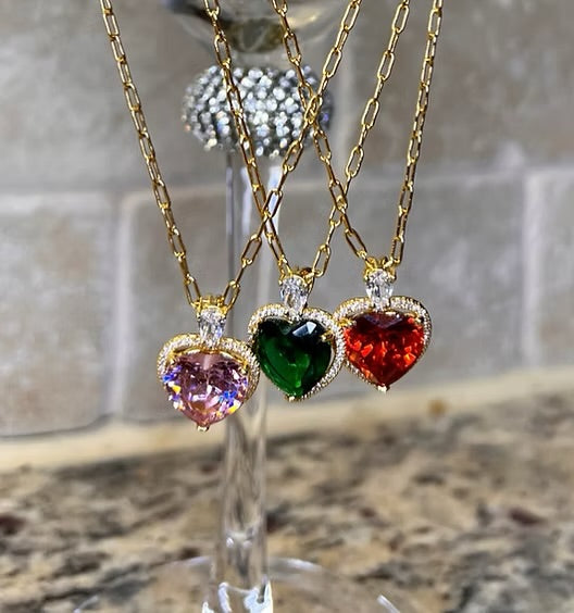 Three heart-shaped gemstone necklaces on gold chains with a blurred background.