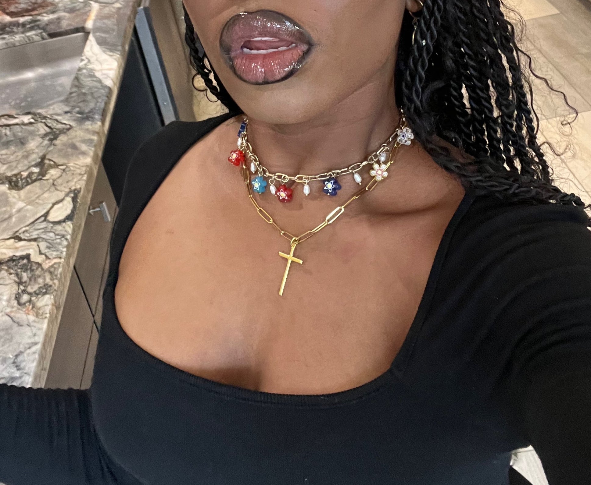 Person wearing a black top and multiple necklaces with a visible background.