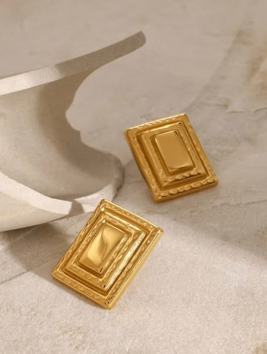Gold square earrings on a textured beige surface