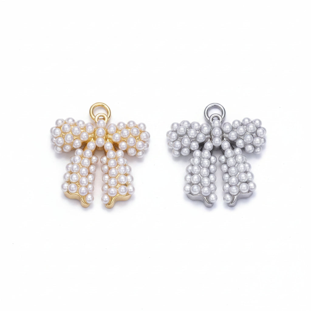 Two pearl bow charms on a light lavender background, one with gold-tone metal and one with silver-tone metal.