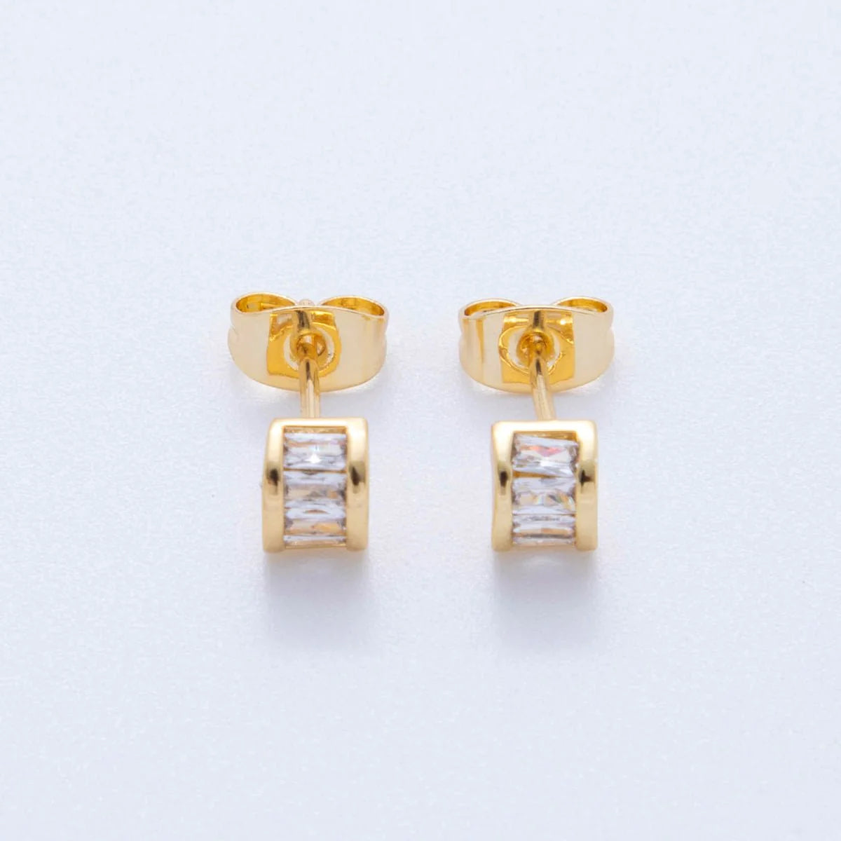 Gold earrings with clear gemstones on a light gray background