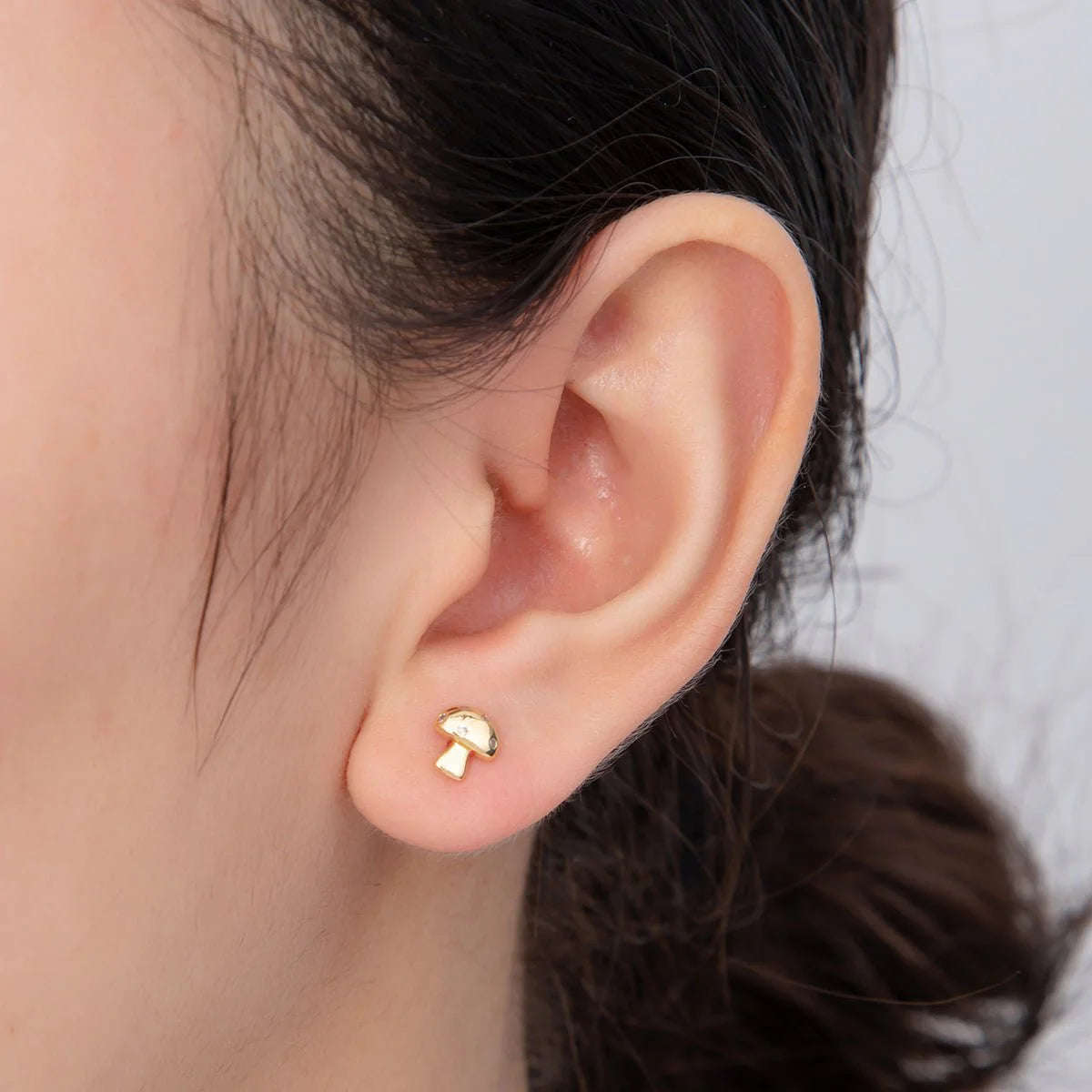 Gold earring worn on a person's ear with a neutral background