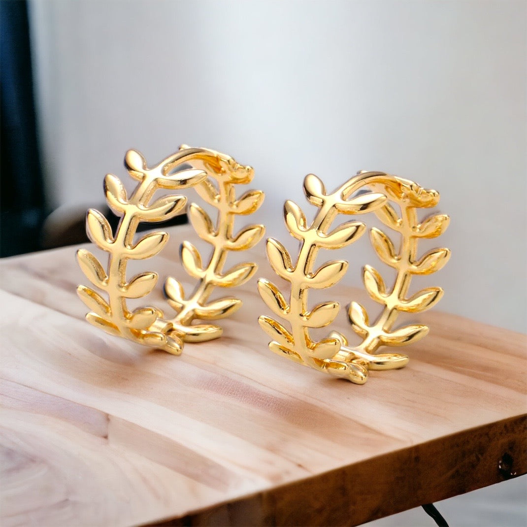 Gold leaf-shaped earrings on a wooden surface with a neutral background