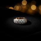 A gold ring with a pavé-set row of clear gemstones, displayed on a black textured surface with warm golden bokeh lights in the background.