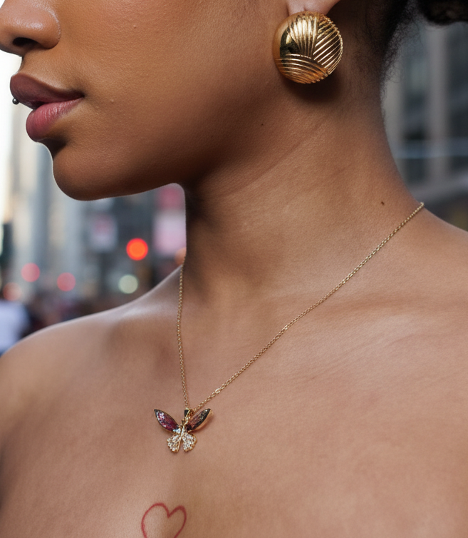 Close-up of a person wearing gold earrings and a necklace with a butterfly pendant.