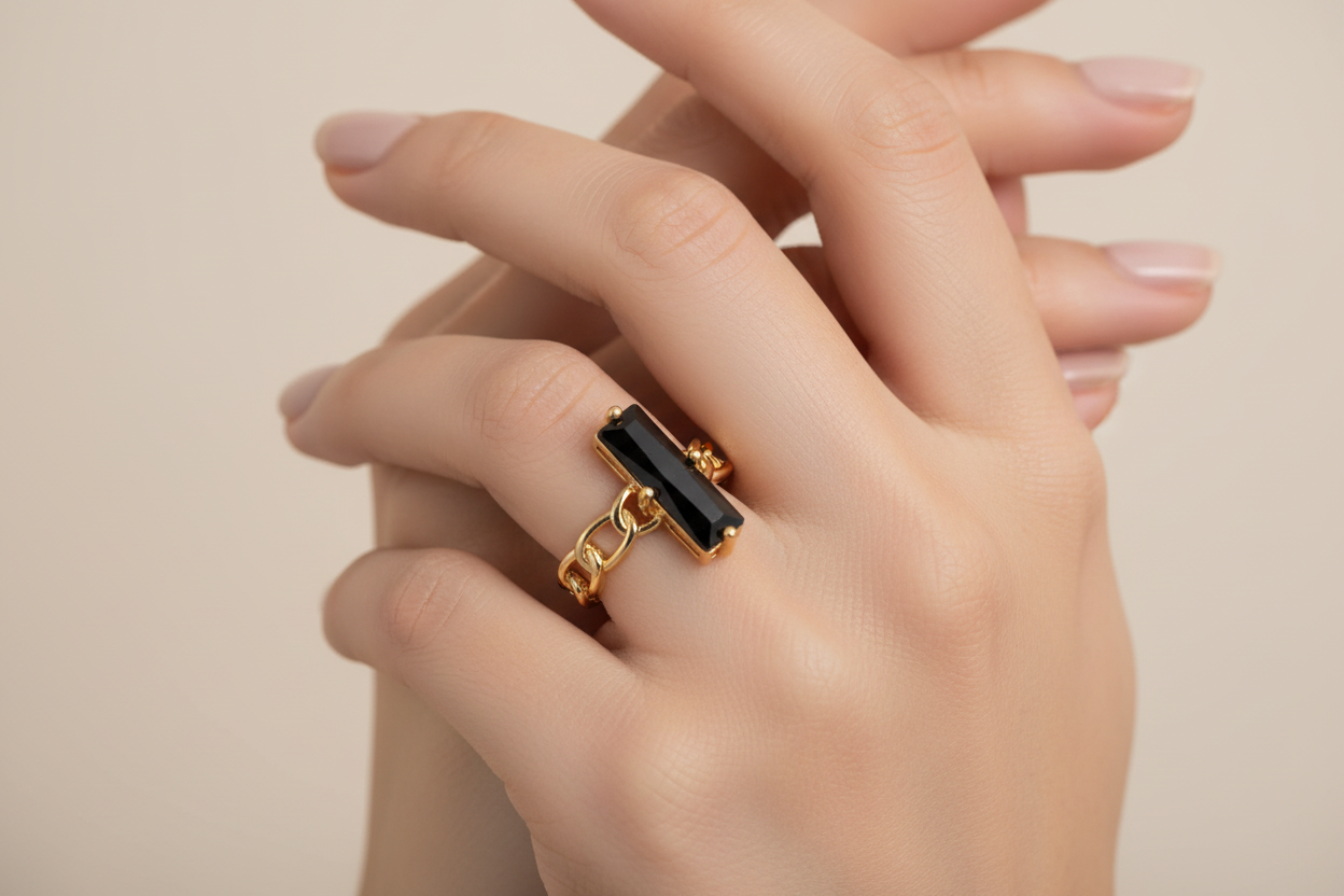 Gold ring with a black stone on a hand against a neutral background